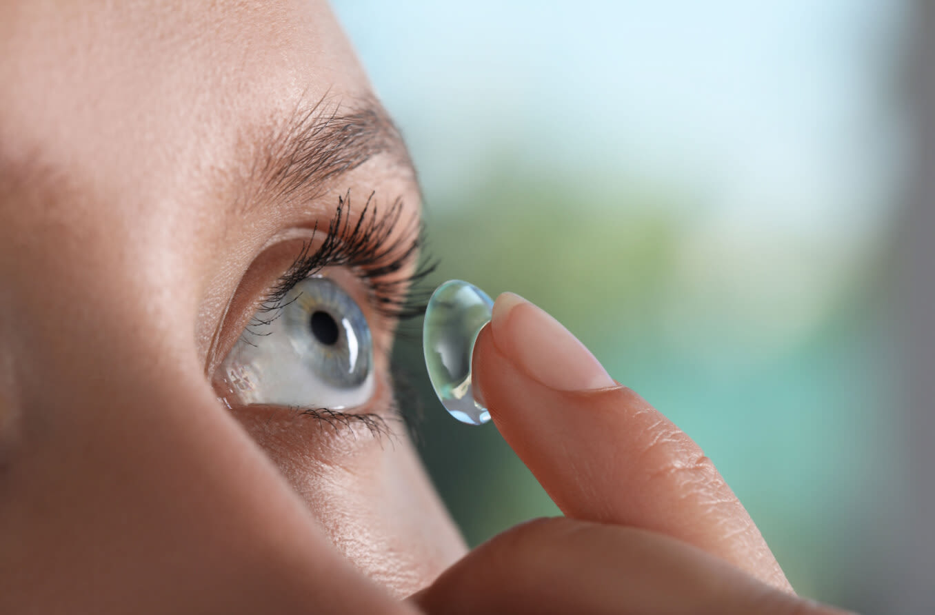 Young woman putting contact lens in her eye.